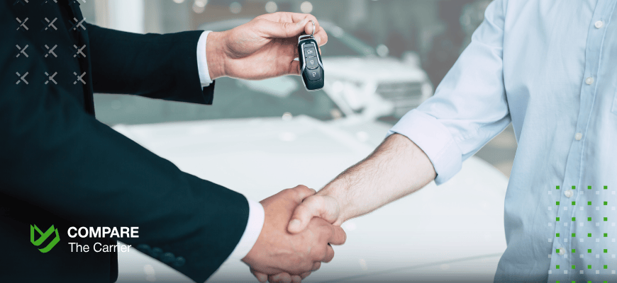 pros of buying a car online Close-up of two people shaking hands while one person is handing car keys to the other, symbolizing the completion of a car purchase transaction, with a car showroom in the background. The Compare The Carrier logo is visible.