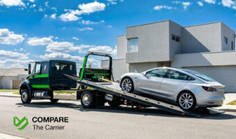 Professional flatbed tow truck winching a silver electric sedan onto the deck on a bright, clean residential street.